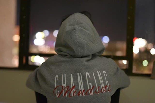 Person in a hoodie with Changing Mindsets text, looking out at city lights